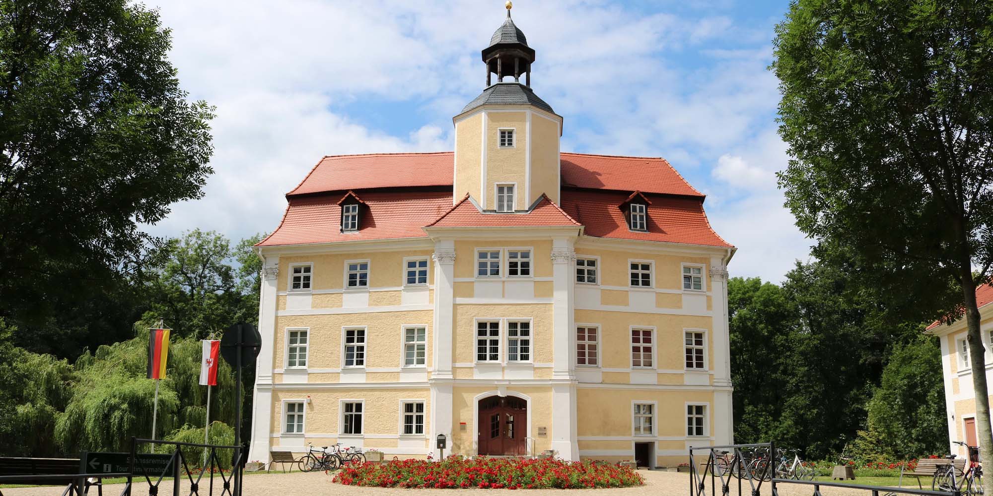 Das Stadtdschloss in Vetschau, ein gelbes Schloss mit ziegeldach und davor ein Blumenbeet